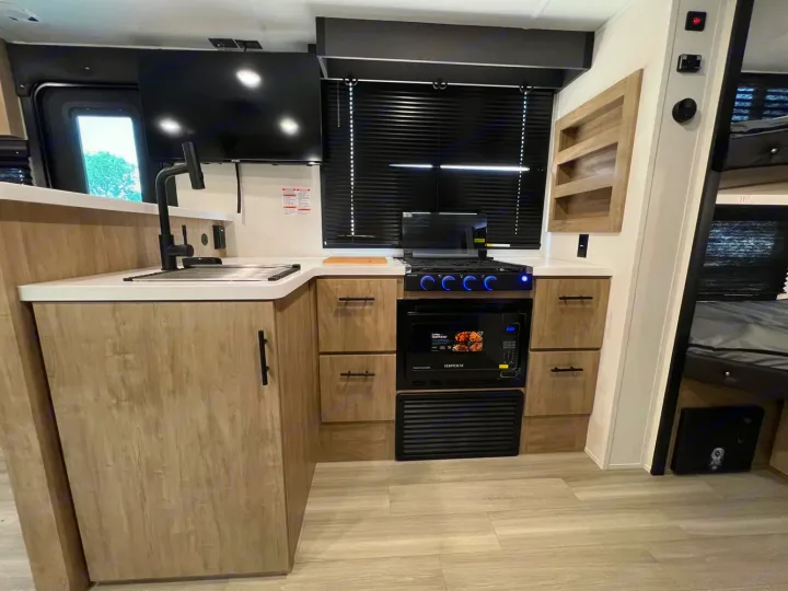 Compact RV rental kitchen: modern sink, stove, microwave, light wood cabinets, and TV, providing full amenities for travel.. Forest River Campsite Reserve 2026