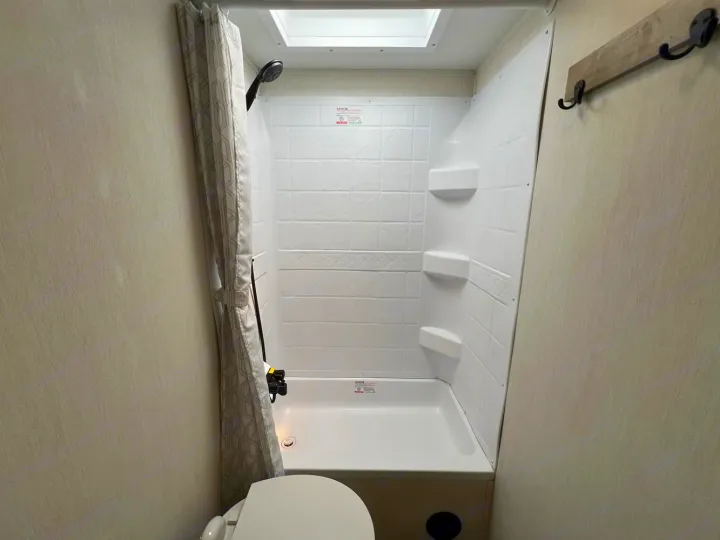 This RV rental offers a functional and clean shower stall with a skylight and wall hooks, part of a compact bathroom.. Forest River Campsite Reserve 2026