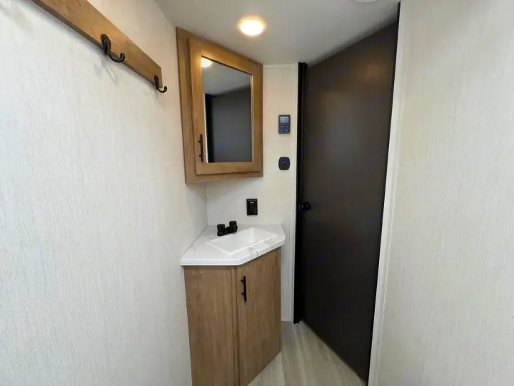 Compact RV rental bathroom with a corner sink vanity, medicine cabinet, coat rack, and a dark door.. Forest River Campsite Reserve 2026
