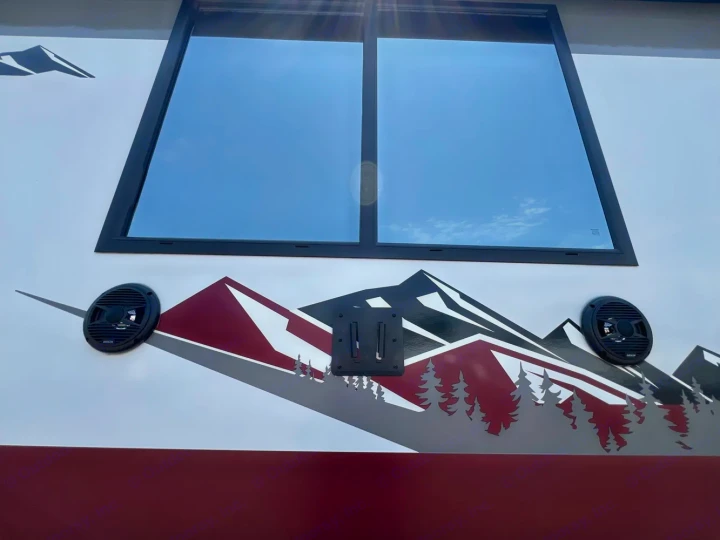RV rental side featuring a mountain decal, external speakers, and a TV mount below a large window. Perfect for outdoor adventures!. Forest River Campsite Reserve 2026