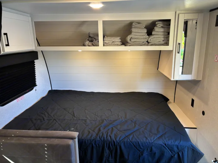Compact RV rental bedroom featuring a comfy bed, overhead storage cabinets, and an exit window for safe travels.. Jayco Jay Flight SLX 2026
