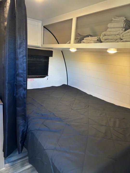 Cozy RV rental bedroom with a dark comforter, overhead storage shelves for linens, and a privacy curtain.. Jayco Jay Flight SLX 2026