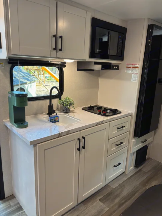 Compact RV rental kitchen with modern white cabinets, marble-look countertop, Keurig, stovetop, and microwave.. Jayco Jay Flight SLX 2026