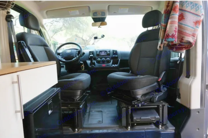 RV rental van interior: Swivel driver & passenger seats, dashboard, and custom fridge cabinet on the left.. Dodge Ram 1500 2021