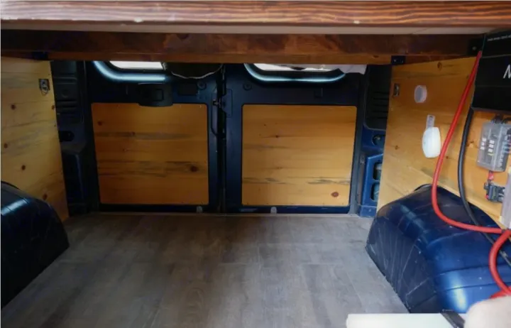 RV rental camper van interior, showing under-bed storage, wood paneling, electrical setup, and laminate flooring.. Dodge Ram 1500 2021
