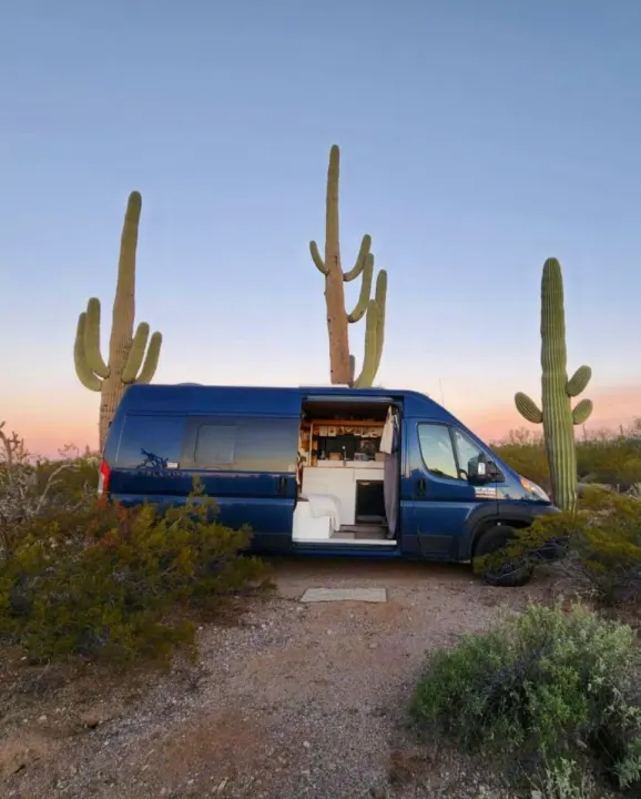 Blue rv rental van in desert with saguaro cacti, door open revealing interior. Sunset hues.. Dodge Ram 1500 2021