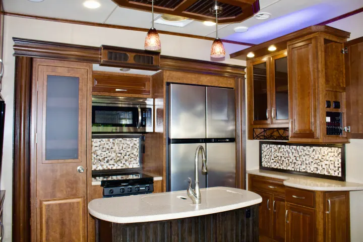 Spacious RV rental kitchen featuring rich wood cabinets, stainless steel appliances, a large counter, and decorative lighting.. Grand Design Solitude 2015