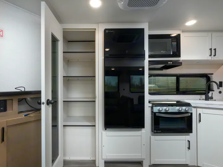 Modern RV rental kitchen with open pantry, black fridge, microwave, oven, & sink. Clean, organized interior for travel.. Jayco Jay Flight 2026