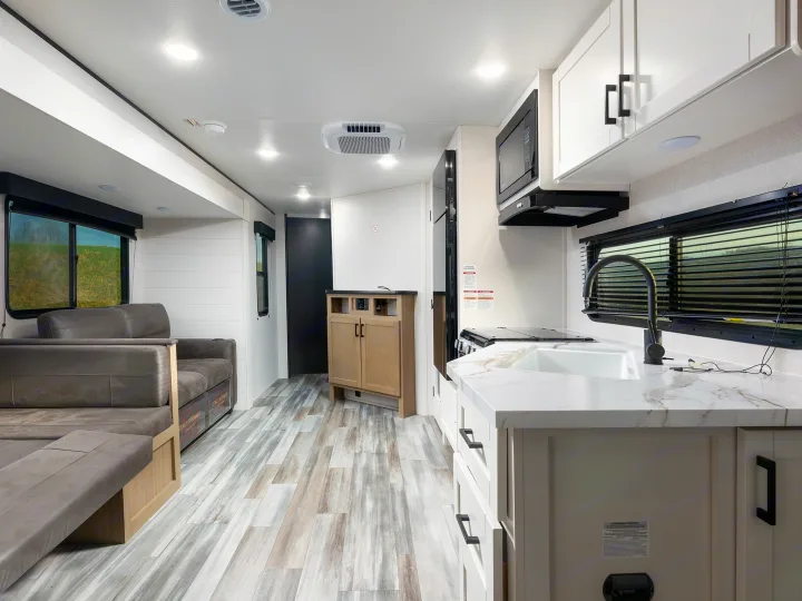 Bright, modern rv rental interior showcasing a kitchen with white cabinets, a sink, and a comfortable gray sofa. Perfect for road trips.. Jayco Jay Flight 2026