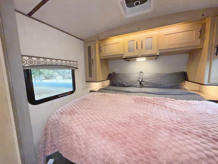 Cozy rv rental bedroom interior features light wood cabinets, a plush pink blanket, and a window with an outdoor view.. Cruiser RV Radiance Ultra Lite 2020