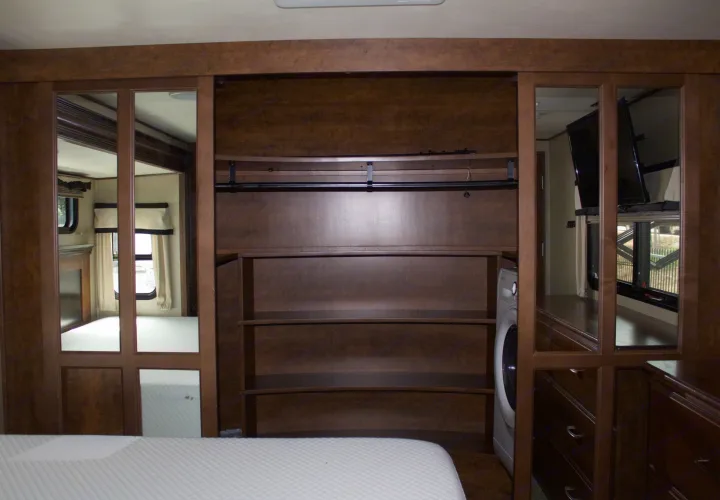 RV rental bedroom: mirrored closets reflecting windows, a bed, and TV. Central storage with shelves, hanging rod, and a washing machine.. Grand Design Solitude 2015
