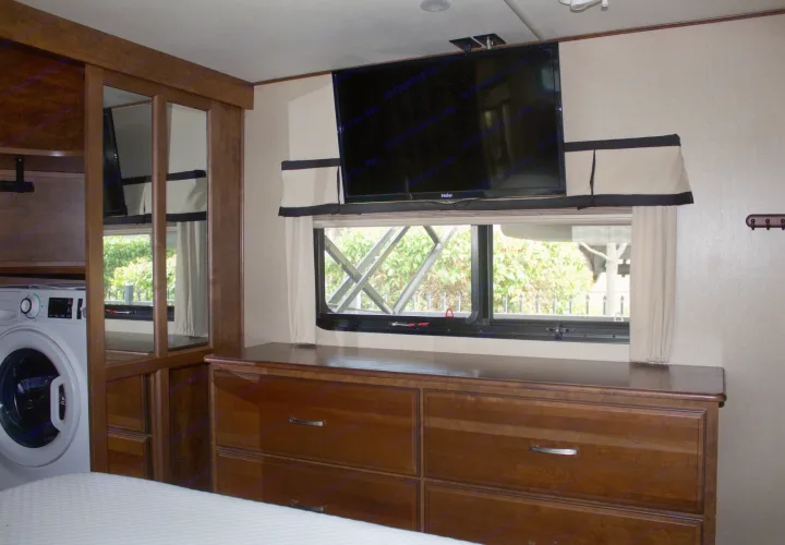 This RV rental bedroom offers comfort with a mounted TV, window, wood dresser, and a convenient washing machine.. Grand Design Solitude 2015