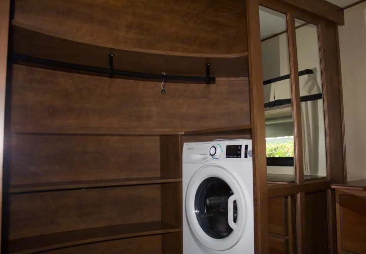 RV rental convenience: A built-in Splendide washer/dryer combo in a wood-paneled closet with shelves and hanging rod.. Grand Design Solitude 2015