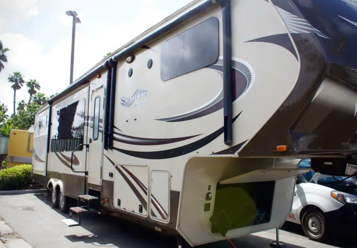 A spacious Grand Design Solitude fifth-wheel RV rental in tan and brown, parked on asphalt with steps out.. Grand Design Solitude 2015