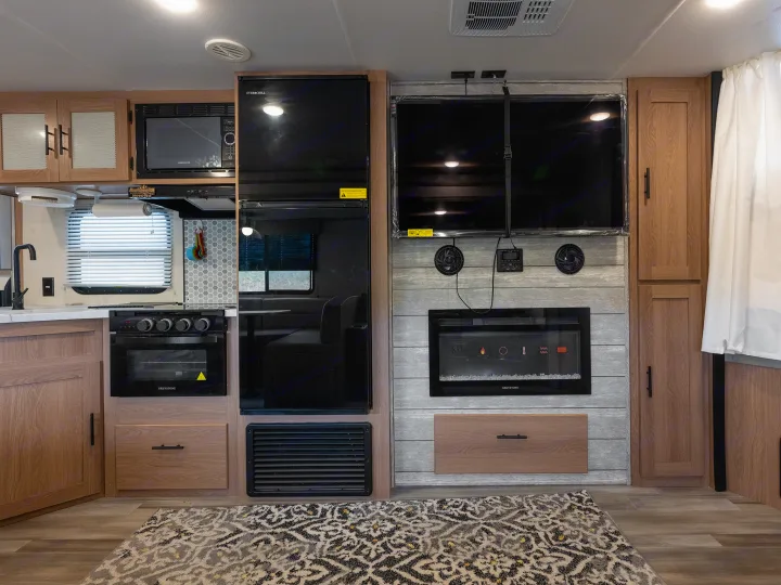 RV rental's modern interior: kitchen with fridge, microwave, oven, and living area with dual TVs, fireplace, and cabinets.. Prime Time Avenger 2024