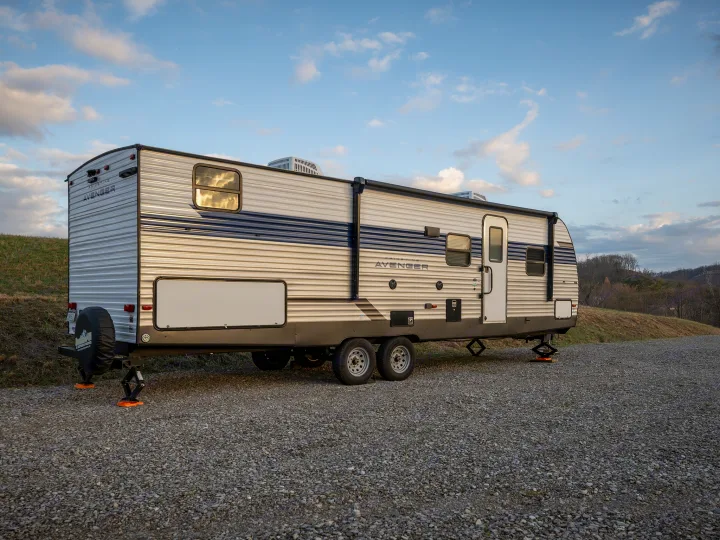 This Primetime Avenger rv rental travel trailer is set up on a gravel site under a blue sky, ready for camping.. Prime Time Avenger 2024