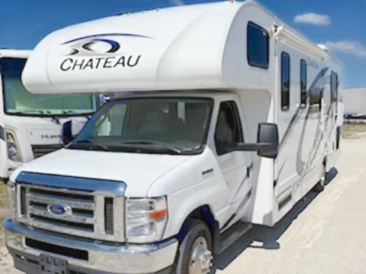 This white Thor Chateau Class C rv rental, a compact motorhome with a distinctive cab-over bunk, parked outdoors.. Thor Chateau 2023