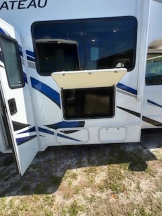 This white RV rental features an outdoor TV in an open compartment for campsite entertainment. An open door invites you inside.. Thor Chateau 2023