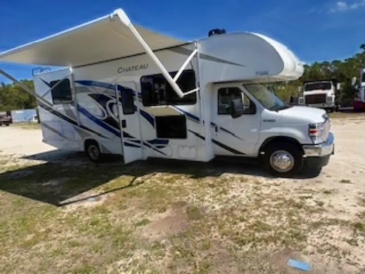 This white Chateau Class C RV rental, with its awning extended, awaits adventure on a sunny, open lot.. Thor Chateau 2023