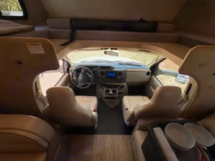 From inside your rv rental: view of the driver's cab, steering wheel, front seats, and overhead bunk.. Thor Chateau 2023