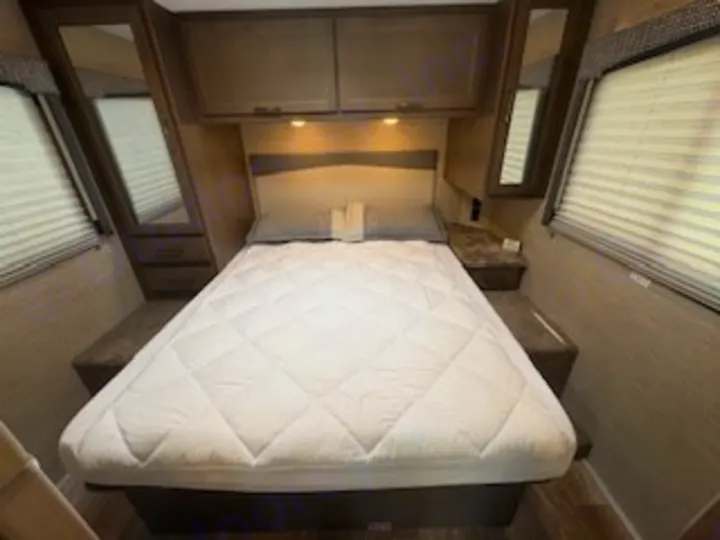 This cozy RV rental bedroom features a queen bed with a quilted mattress, overhead storage, and mirrors for comfort on the road.. Thor Chateau 2023