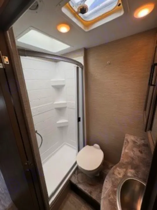 RV rental bathroom with compact shower, toilet, and vanity sink, lit by a skylight.. Thor Chateau 2023