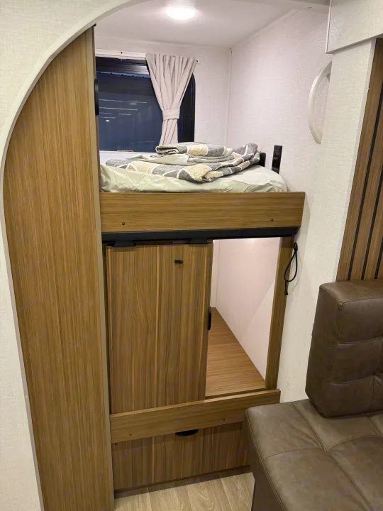 This RV rental interior features a modern bunk bed over storage, with an adjacent brown sofa. Perfect for compact living.. Forest River Salem Cruise-Lite 2026