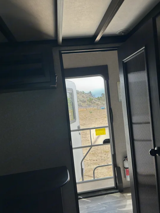 RV rental interior view through the open screen door to a dry, natural landscape. Fire extinguisher visible, ready for your adventure.. Jayco Eagle 2022