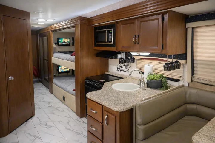 Modern rv rental featuring a well-equipped kitchen, cozy dining nook, and bunk beds with individual TVs, perfect for family adventures.. Thor A.C.E 30.2 2014