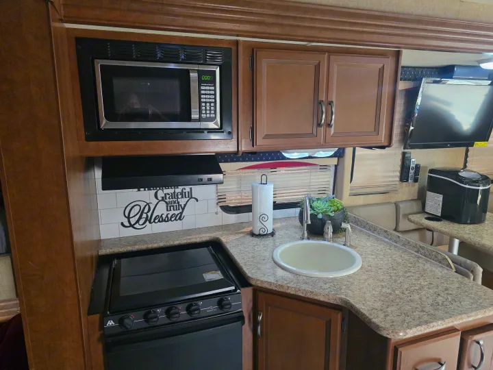 Compact RV rental kitchen with microwave, stove, sink, and speckled counter. Wood cabinets and 'Grateful and Blessed' backsplash.. Thor A.C.E 30.2 2014
