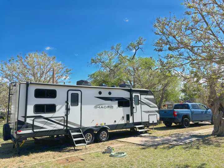 Enjoying an outdoor adventure with this rv rental! A white Imagine travel trailer and blue pickup truck are set up at a shady campsite.. Grand Design Imagine 2022