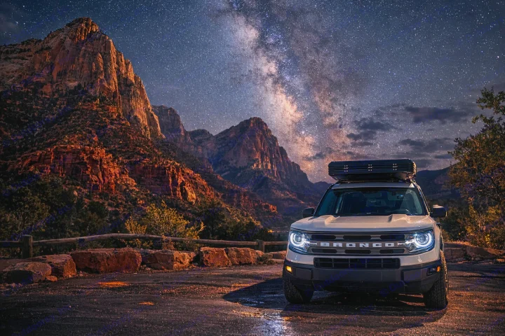 A white Bronco with glowing headlights & rooftop tent under the Milky Way over red mountains. Ideal RV rental adventure.. Ford Bronco Sport 2024