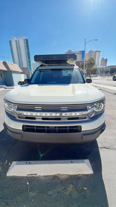 White Ford Bronco Sport with a rooftop tent, parked in a sunny urban lot. A versatile option for an exciting rv rental adventure.. Ford Bronco Sport 2024