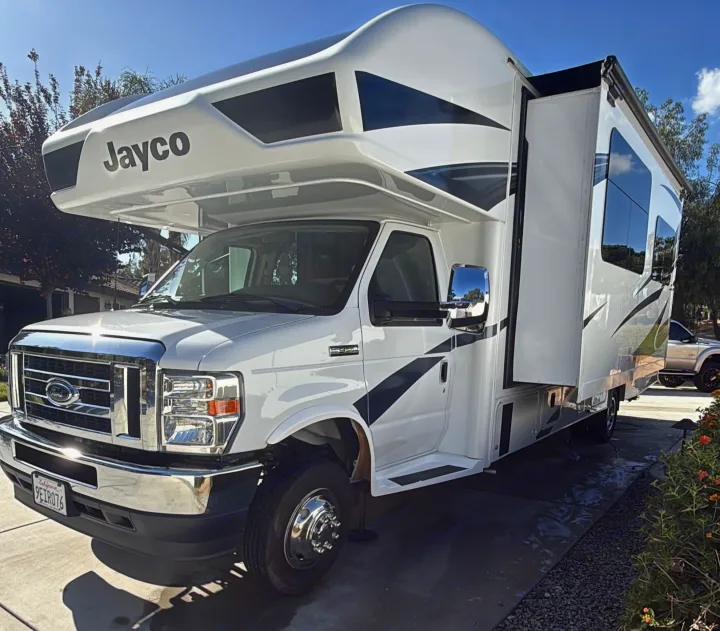 Bright white Jayco RV rental parked on a sunny driveway, showcasing its extended slide-out.. Jayco Greyhawk 2023