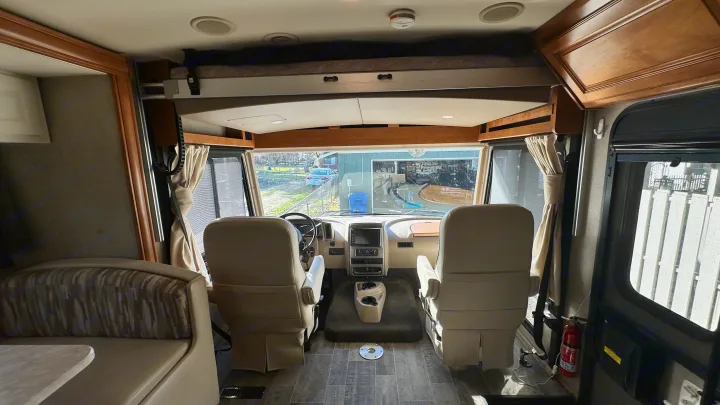 Inside an RV rental: view of the spacious cockpit with driver/passenger seats, dashboard, and overhead bunk. Ready for your journey.. Winnebago Vista LX 2019
