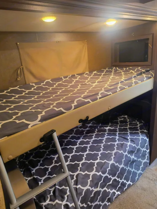 RV rental bunk beds with grey patterned bedding and ladder, offering a compact sleeping space in a cozy interior.. Thor Motor Coach Freedom Elite 2019