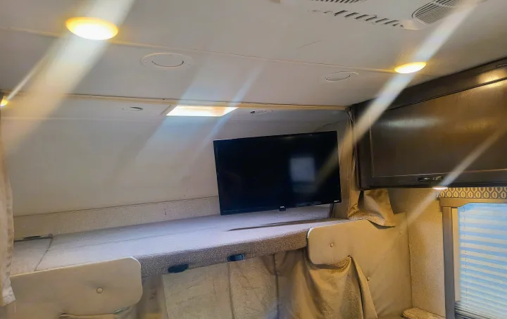 RV rental overhead bunk with TV, ceiling lights, and air vents, providing a compact sleeping area in a camper.. Thor Motor Coach Freedom Elite 2019