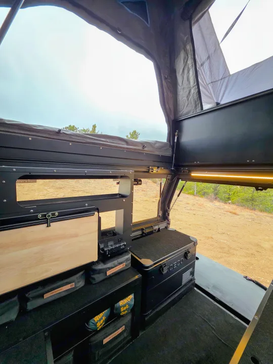 Interior of an overland RV rental camper with modular storage, a fridge, and a pop-top tent, ready for adventure.. Dirtbox Overland Canopy Camper 2023