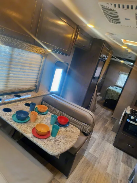 This RV rental interior features a dinette with colorful dishes, overhead cabinets, and a peek into the bedroom.. Thor Motor Coach Freedom Elite 2019