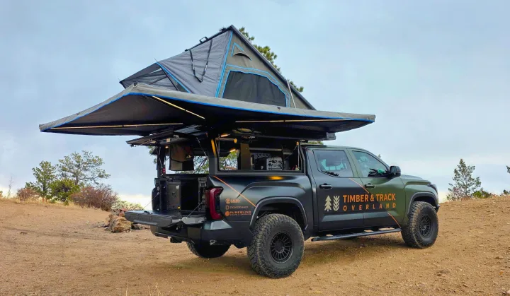 Dark green overland truck with deployed rooftop tent & awning on a dirt path. Ideal RV rental for off-grid camping adventures.. Dirtbox Overland Canopy Camper 2023