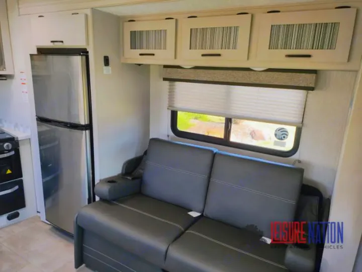 RV rental: Modern interior featuring a stainless steel fridge, kitchen, and a comfortable gray sofa by a window.. Coachmen Freelander 2023