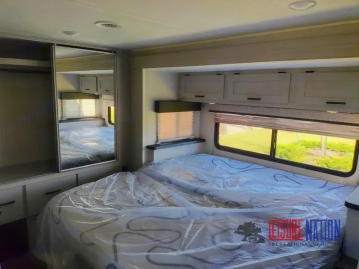 Clean RV rental bedroom featuring a large bed, mirrored closet, and overhead cabinets for a comfortable stay.. Coachmen Freelander 2023