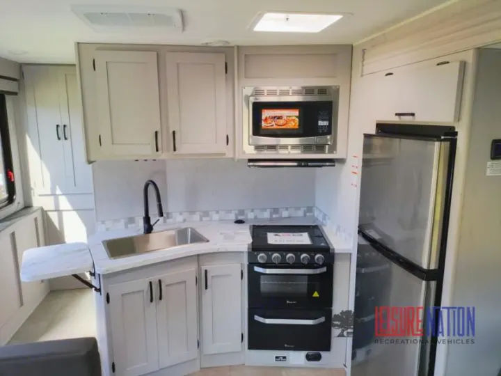 RV rental kitchen with light cabinets, stainless sink, microwave, stove, fridge, and extendable counter.. Coachmen Freelander 2023
