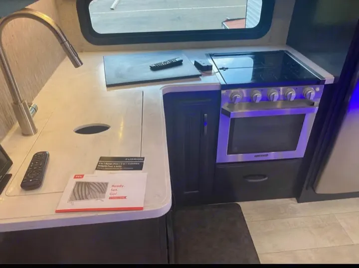 RV rental kitchen featuring a modern sink, counter space, and a stainless steel oven/stove combo. Perfect for cooking on the road.. Grand Design Momentum 2019