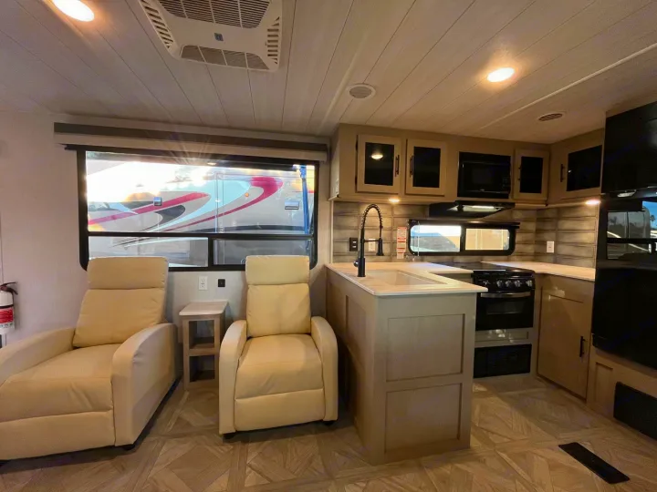 Modern RV rental interior showing a kitchen with sink & stove, plus two comfy recliners in the living area.. Forest River Salem 2023
