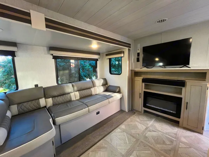 This rv rental living area offers a comfy L-shaped sofa, windows, TV, and electric fireplace, perfect for relaxing after exploring.. Forest River Salem 2023