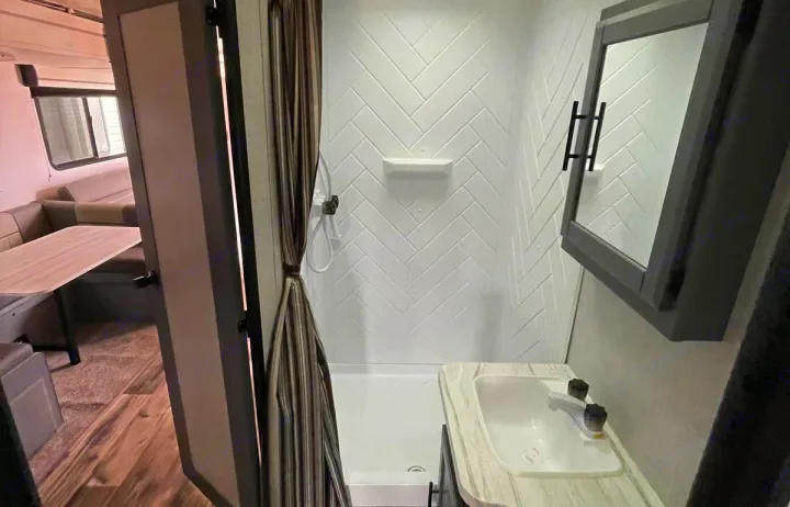 RV rental interior: A bright bathroom with a chevron-tiled shower, sink, and vanity. Dinette visible beyond the door.. Crossroads RV Volante 2023