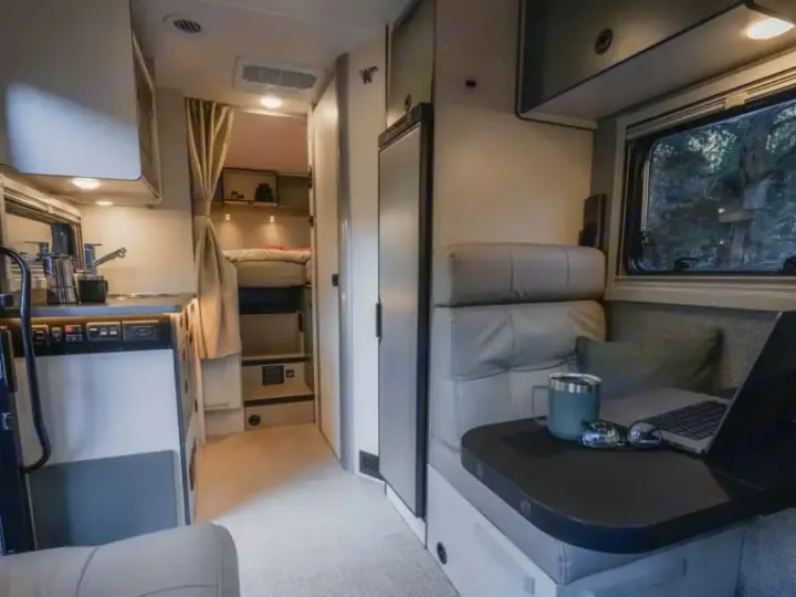 Modern rv rental interior featuring a compact kitchen, comfortable seating with laptop, and sleeping area.. Winnebago Ekko 2025