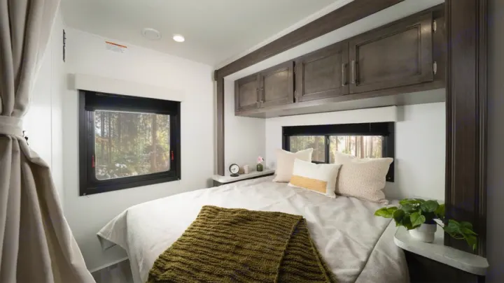 Cozy RV rental bedroom with forest views, a comfortable bed, and overhead storage, featuring white walls.. Entegra Odyssey SE 2026