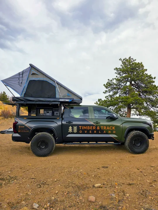 A green & black overland truck, branded 'Timber & Track Overland', with a rooftop tent. An ideal rv rental for off-grid camping.. Dirtbox Overland Canopy Camper 2023